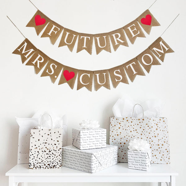Customize this Future Mrs. Banner with the bride to be&#39;s new last name! The top layer spells out the word Future in white letters with a red heart on either side. The bottom layer spells out the word Mrs. followed by a red heart and then an option to personalize this banner with the bride&#39;s new last name.