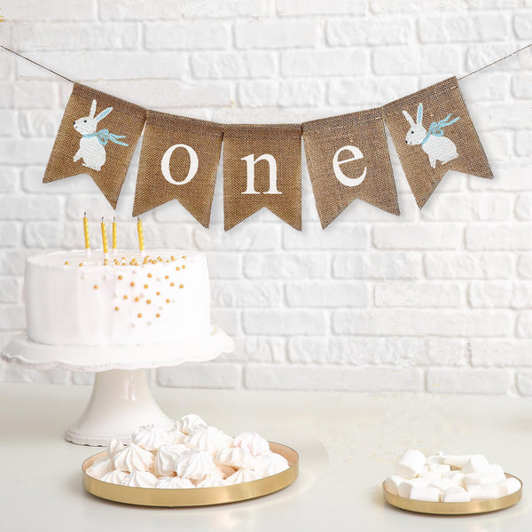One first birthday burlap banner. This banner has 2 adorable hand stenciled white bunnies wearing a blue ribbon. The word one is written on the flags in white lowercase font.