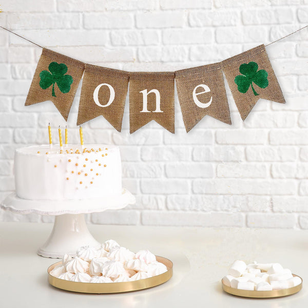 This is a burlap banner that has 5 fishtail shaped flags. It has ONE spelled out in white lowercase letters on the three middle flags. There are green hand painted clovers on either end of the banner.