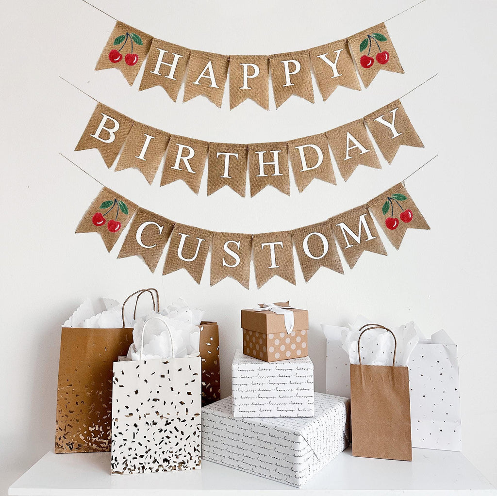This is a burlap banner made out of 4 inch by 6 inch fishtail flags. It is on three strings. The top string has the word Happy in white letters with an image of a cherry on either end. The second string has the word Birthday in white letters. The top string has the word CUSTOM in white letters with an image of a cherry on either end.