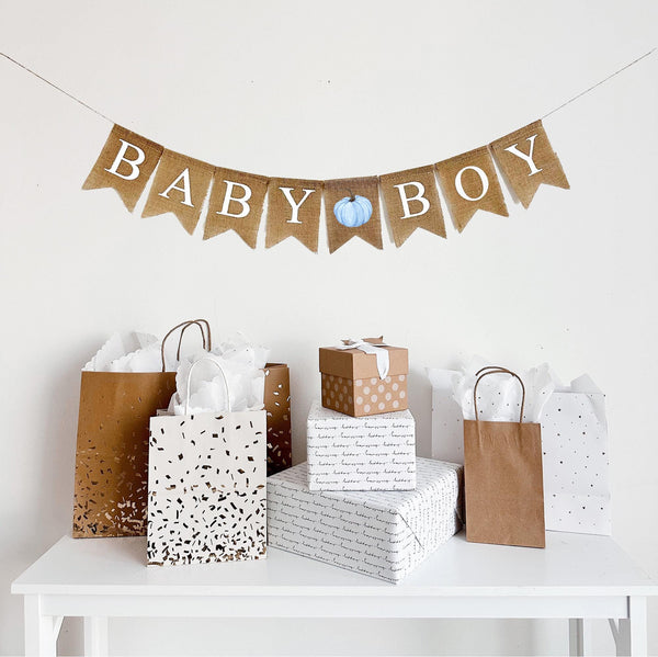 A burlap banner made from 4.5 by 6.5 inch fishtail shaped flags. Each flag has a pocket across the top for stringing. This banner says BABY BOY in white capital letters. There is a printed image of a light blue watercolor pumpkin with a brown stem between each word. It is strung on a jute string that is 110 inches in length.