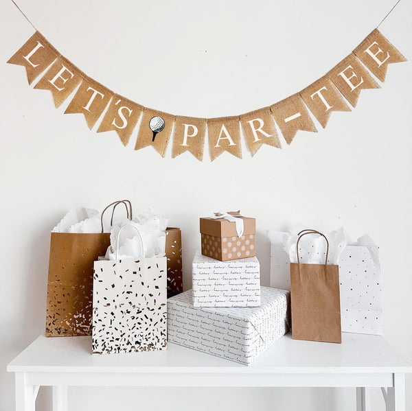 A burlap banner made from 4.5 by 6.5 inch fishtail shaped flags. Each flag has a pocket across the top for stringing. It says LET&#39;S PAR-TEE in white capital letters with a dash between PAR and TEE. There is an image of a white golf ball sitting on a black tee in between the words. It is strung on a jute string that is 110 inches in length.