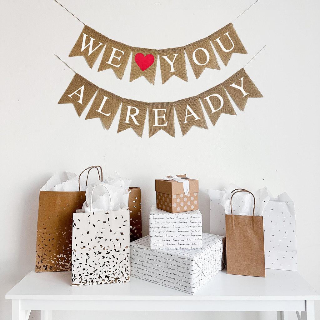 A burlap banner reading We &quot;Heart&quot; You Already with a red heart image between the words WE and YOU.