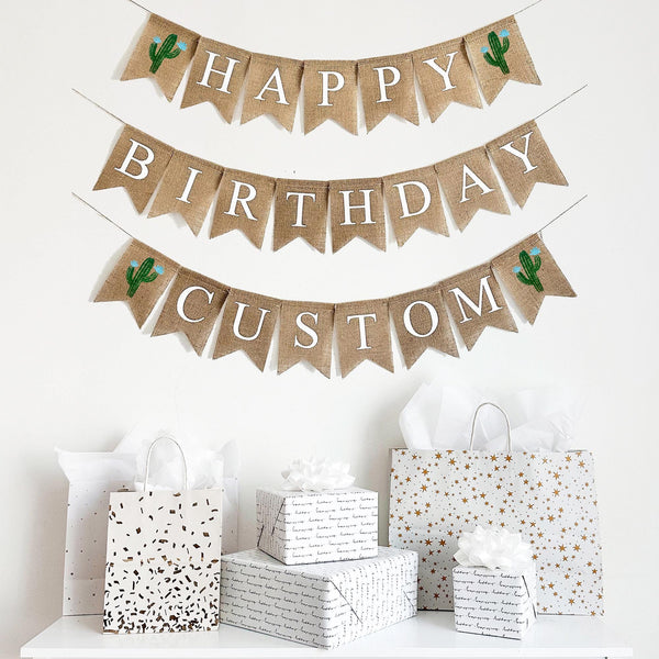 A happy birthday burlap banner strung on two or three strings. The top row reads &quot;HAPPY&quot; with a hand painted green cactus with blue flowers on each end of the word. The second line reads &quot;BIRTHDAY&quot;.  The third optional line give your the choice to add a personalization to your banner.  The personalized line also has a cactus with blue flowers on either end of the wording of your choice.