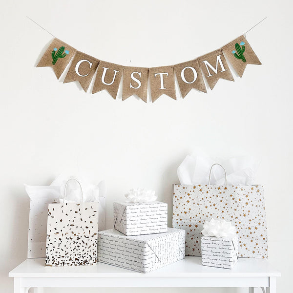 This customizable burlap banner allows you to add a name, date or special saying to add a personalized touch to your event. On each end of your custom wording, there is a hand stenciled green cactus with blue flowers.