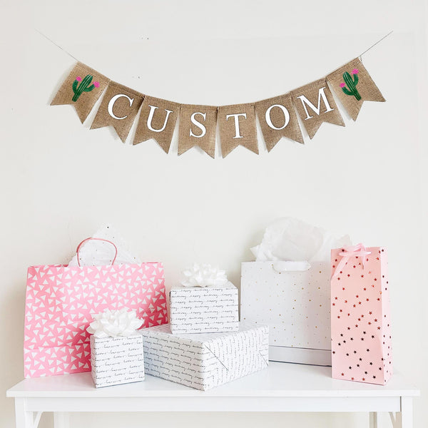 This customizable burlap banner allows you to add a name, date or special saying to add a personalized touch to your event. On each end of your custom wording, there is a hand stenciled green cactus with pink flowers.