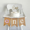 This burlap high chair banner includes three 5 x 7 burlap flags spelling out O N E. The O on this banner is a pink sprinkled donut.