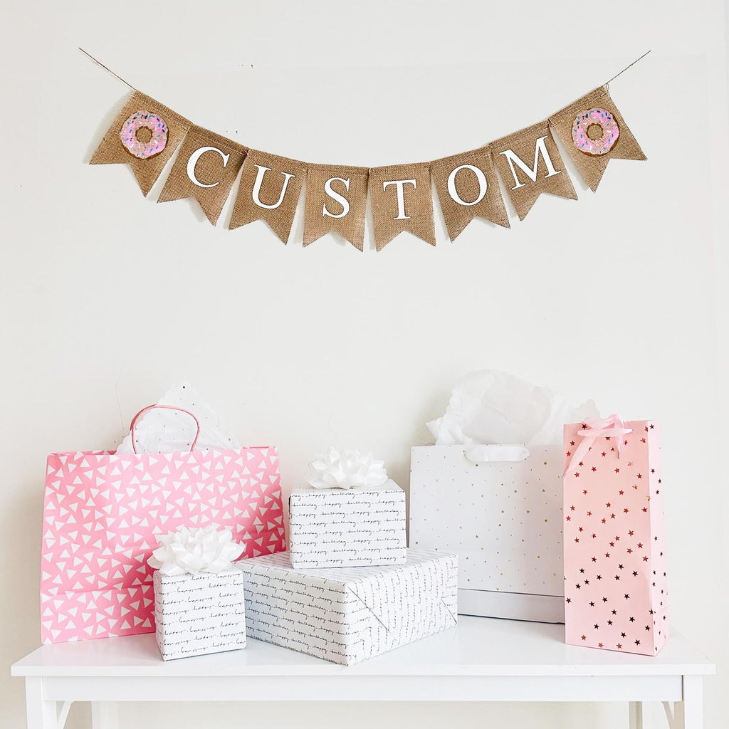 Customize this pink sprinkle donut banner with a name, date or quote to personalize your event. The letters on each flag are in white, uppercase font. This banner is designed with a pink donut flag on the end of your customized wording.