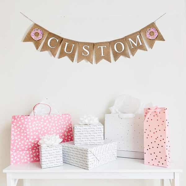 Customize this pink sprinkle donut banner with a name, date or quote to personalize your event. The letters on each flag are in white, uppercase font. This banner is designed with a pink donut flag on the end of your customized wording.