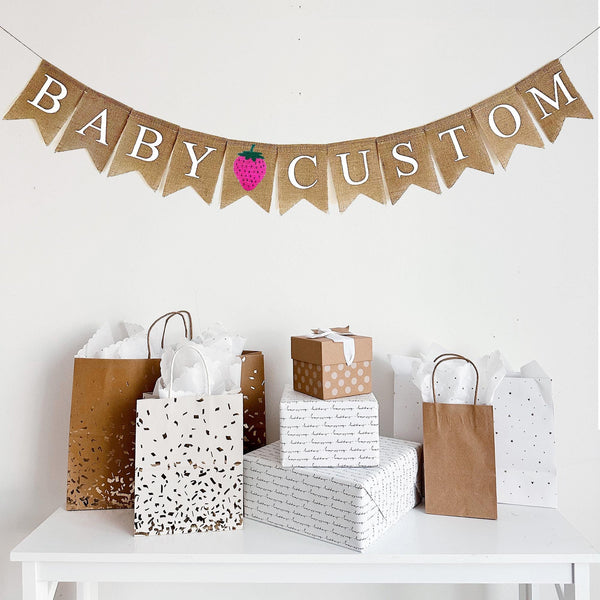 This one tiered banner spells out the word BABY in white letters on fishtail burlap banner flags followed by a pink hand stenciled strawberry. Following the strawberry, you have the option to customize your banner with a name, date or saying to add a personal touch to your baby shower.