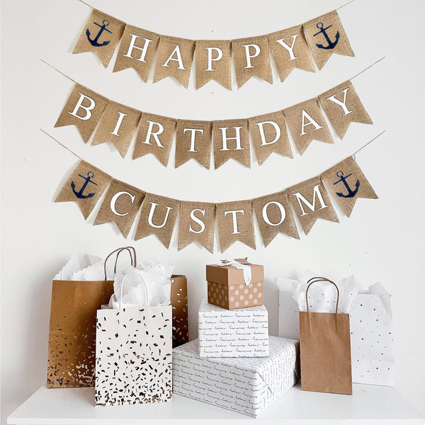 This is a burlap banner made from fishtail shaped flags. Each flag has a white letter painted on it. The top string says HAPPY with a navy anchor on either end. The bottom string says BIRTHDAY. You can add a third row and add a custom name, date or saying to personalize your event. Each flag measures 4.5 by 6.5 inches in size.