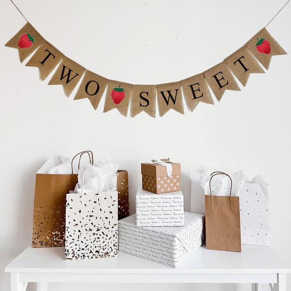 Two Sweet strawberry burlap banner. On one line this burlap banner starts with a red hand stenciled strawberry image followed by burlap flags that spell out the words TWO SWEET with another strawberry in between the two words and then another strawberry at the end.