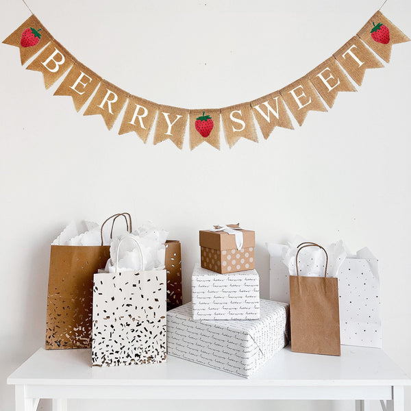 This burlap banner hangs on one string and spells out the words BERRY SWEET in white letters over burlap fishtail flags. Three red hand stenciled strawberry flags stand at the begging, middle and end of the words.