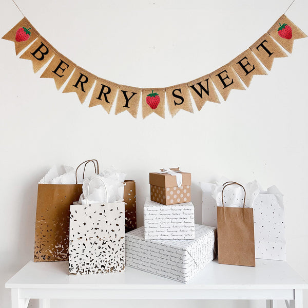This burlap banner hangs on one string and spells out the words BERRY SWEET in black letters over burlap fishtail flags. Three red hand stenciled strawberry flags stand at the begging, middle and end of the words.