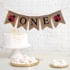A burlap banner that says ONE in black letters with red and black ladybug images on either side of the word.