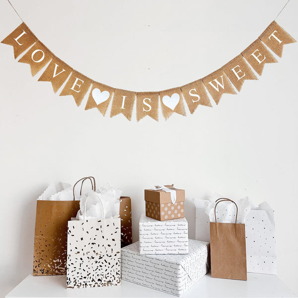This Love Is Sweet banner hangs on one line. The words are written out in white letters with a white heart between Love and Is and another white heart between Is and Sweet.