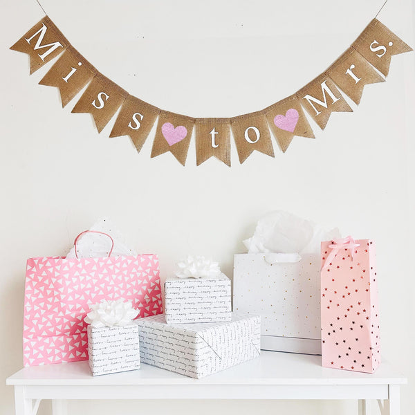 Miss to Mrs burlap banner is written out in white letters on fishtail burlap flags. Between each word there is a hand stenciled pink heart. This banner is perfect for a bridal shower, bachelorette or engagement party.