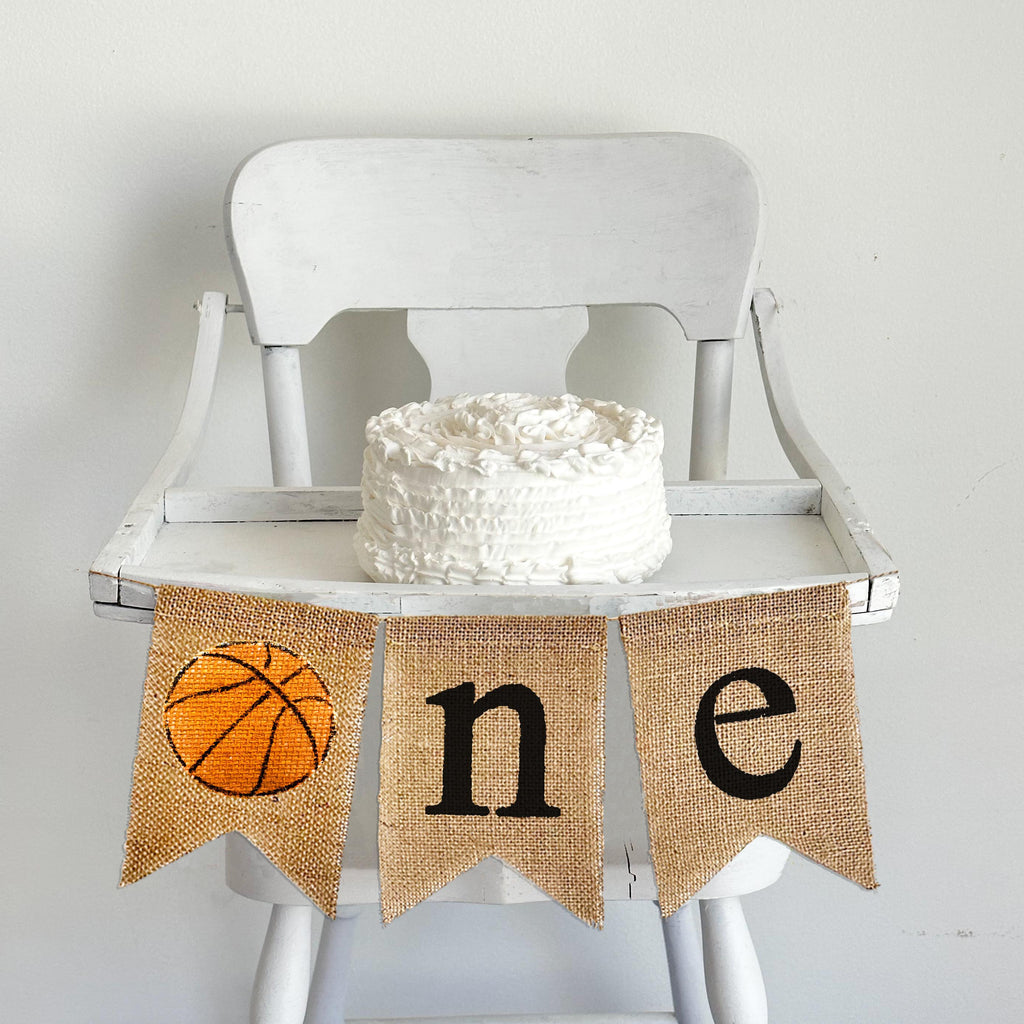 A burlap banner with an orange basketball image and the letters &quot;n&quot; and &quot;e&quot; spelling &quot;one&quot;.