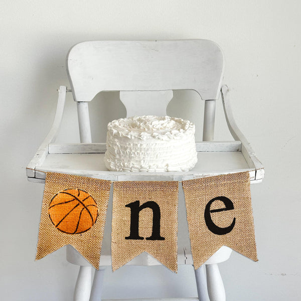 A burlap banner with an orange basketball image and the letters &quot;n&quot; and &quot;e&quot; spelling &quot;one&quot;.
