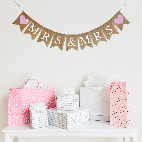 This is a fishtail burlap banner with a letter on each flag spelling out Mrs & Mrs in white letters. On each end of the banner there is a pink heart.