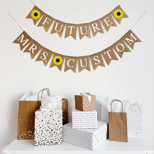 Customize this Future Mrs. Banner with the bride to be&#39;s new last name! The top layer spells out the word Future in white letters with a hand stenciled sunflower on either side. The bottom layer spells out the word Mrs. followed by a sunflower and then an option to personalize this banner with the bride&#39;s new last name.