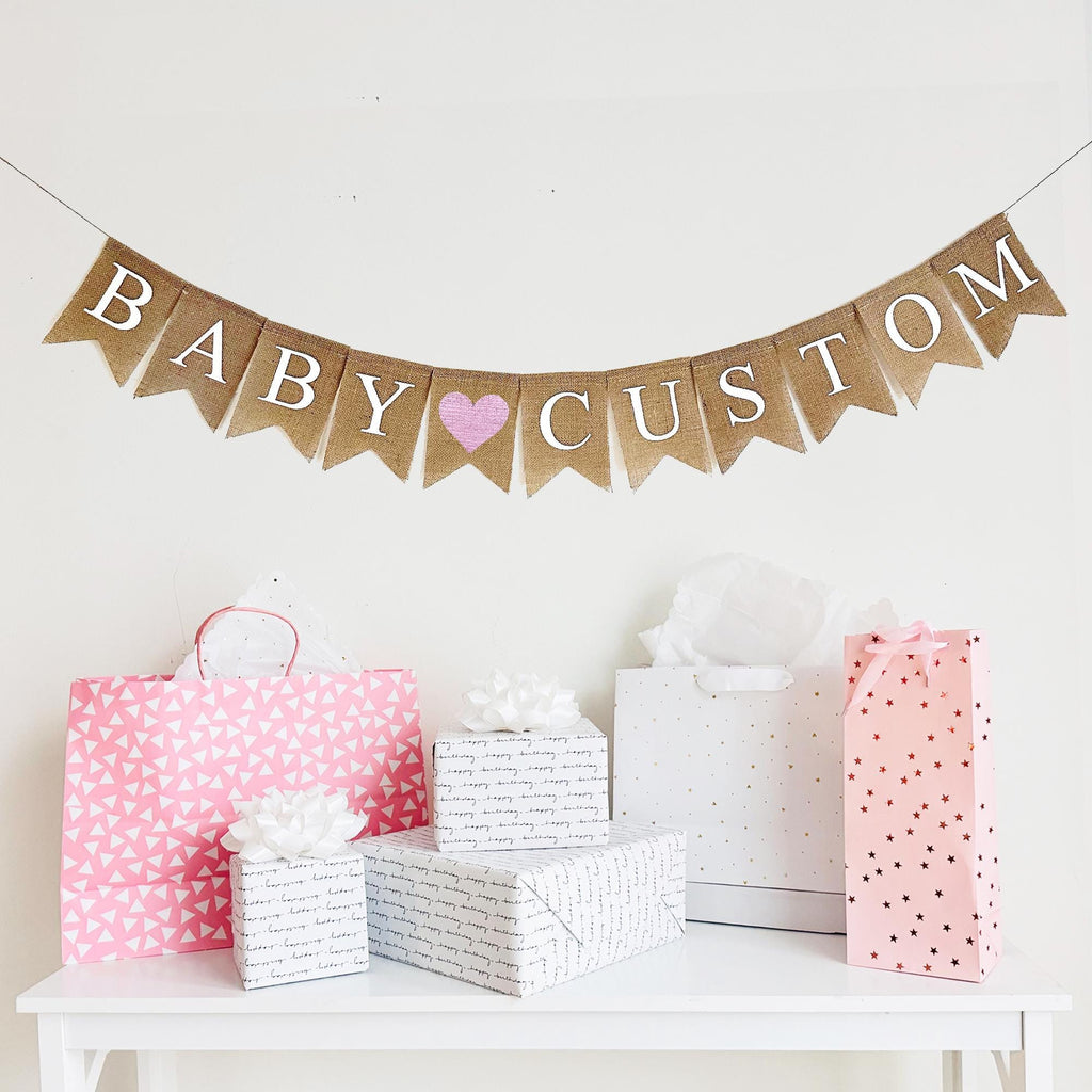 A burlap banner that says baby custom with a pink heart between the words.