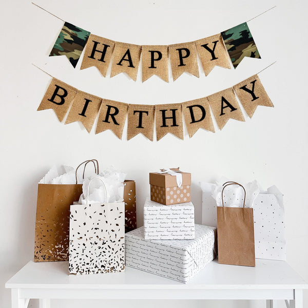 This is a burlap banner is on two lines and spells out the words Happy Birthday on fishtail burlap flags with black letters. The top row reads Happy with two camouflage flags on either end of the word Happy with the word Birthday on the second line. This banner is customizable to add a name, date or saying below the words Happy Birthday.