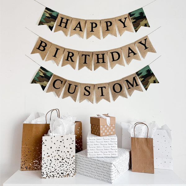 This is a burlap banner is on two lines and spells out the words Happy Birthday on fishtail burlap flags with black letters. The top row reads Happy with two camouflage flags on either end of the word Happy with the word Birthday on the second line. This banner is customizable to add a name, date or saying below the words Happy Birthday.