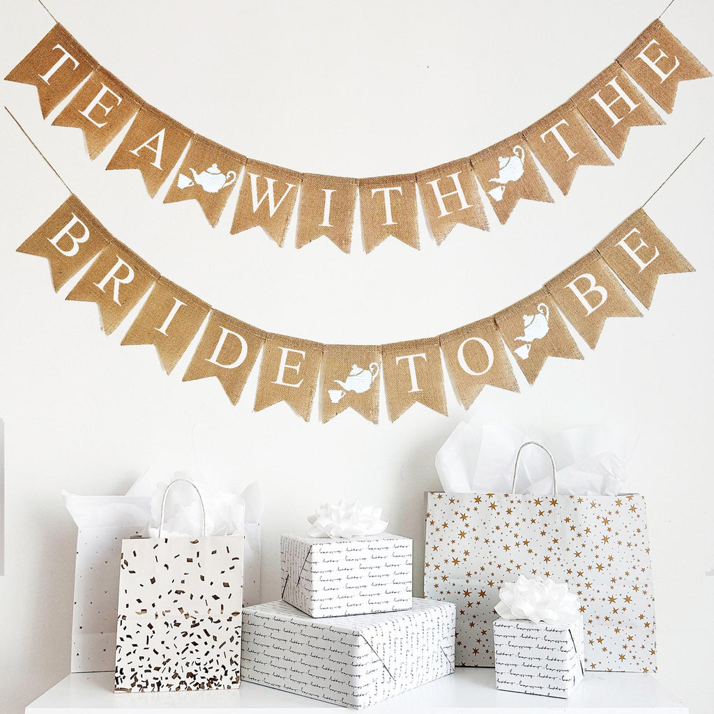 This two tiered burlap banner has white letters on burlap fishtail flags. Each flag measures 4.5 x 6.5. The top layer of the banner reads &quot;Tea With The&quot; and the second line reads &quot;Bride To Be&quot; Between each word is a burlap flag with a hand stenciled tea pot and tea cup. There is a total of 4 image flags on this banner.