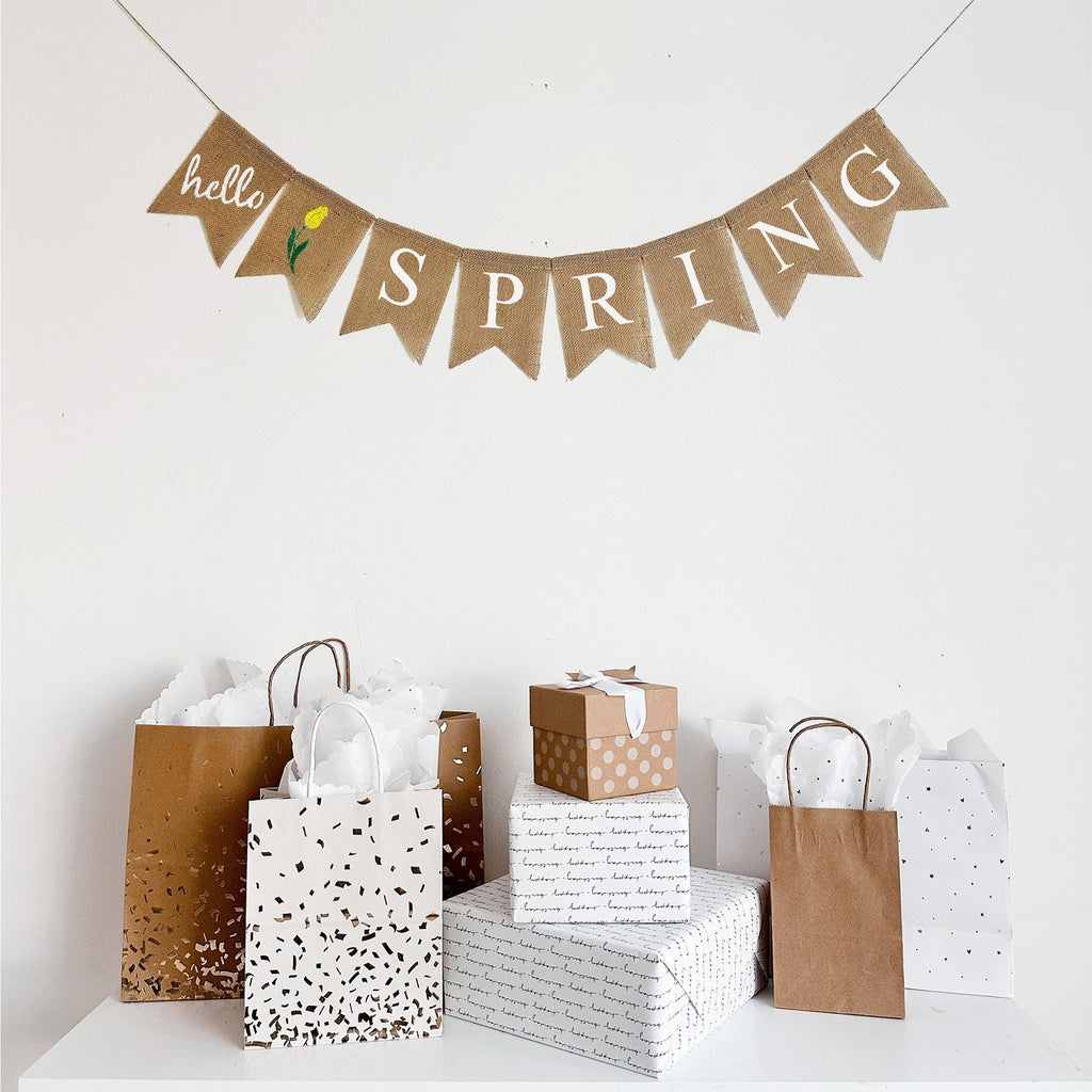 This burlap banner is made up of burlap fishtail flags measuring 4.5 x 6.5. The first flag has the word hello written out in script letters. The second flag is a hand stenciled yellow tulip with the remaining flags spelling out SPRING.