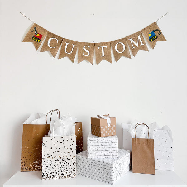 Customize this construction burlap banner with the wording of your choice. Each burlap flag measures 4.5 x 6.5 inches. On either end of the personalized wording, this banner comes with two hand stenciled construction style trucks. One is a red crane and the other is a blue digger.