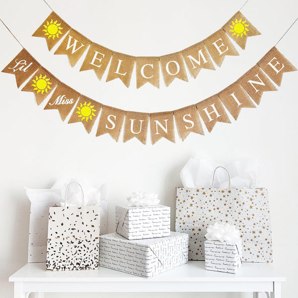 A two tiered banner. On the first tier, the word WELCOME is written out on each flag in white letters with a hand stenciled yellow sun on either end of the word. On the second tier, the banner starts with a flag that says the word &quot;Lil&#39;&quot; in small script letters on one flag followed by a yellowhand stenciled sun, then the word &quot;Miss&quot; also in small script lettering on one single flag, followed by another yellow sun. Following that, the rest of the flags spell out the word s