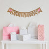 A burlap banner made from 4.5 by 6.5 inch fishtail shaped flags. Each flag has a pocket across the top for stringing. Add a custom name or word of your choice in white capital letters. There is a hand stenciled image of a pink pig on each end of the word. It is strung on a 110 inch jute string.