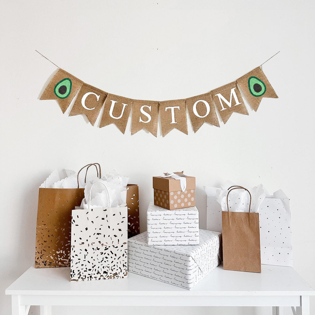 A burlap banner with the word CUSTOM in white lettering between two avocado image flags.