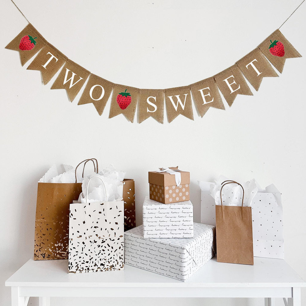 Two Sweet strawberry burlap banner. On one line this burlap banner starts with a red hand stenciled strawberry image followed by burlap flags that spell out the words TWO SWEET with another strawberry in between the two words and then another strawberry at the end.