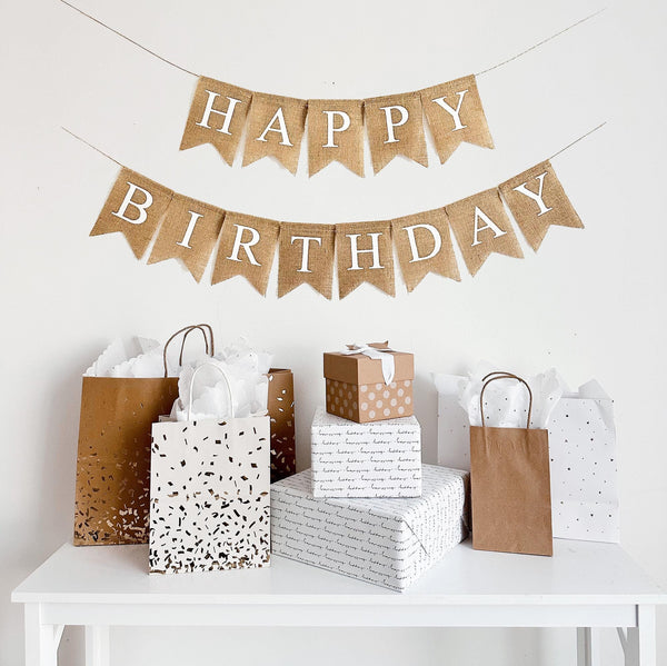 A two tiered burlap banner. The first tier reads happy, second tier reads birthday. The lettering is all white capital letters.