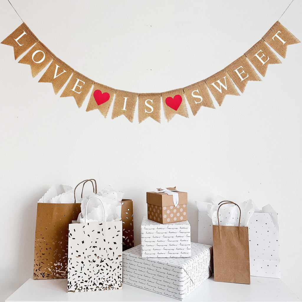 This Love Is Sweet banner hangs on one line. The words are written out in white letters with a red heart between Love and Is and another red heart between Is and Sweet.