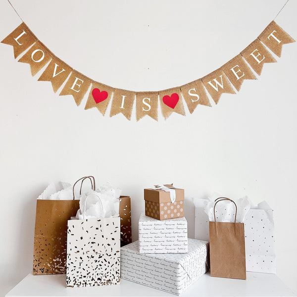 This Love Is Sweet banner hangs on one line. The words are written out in white letters with a red heart between Love and Is and another red heart between Is and Sweet.
