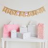 A burlap banner made from 4.5 by 6.5 inch fishtail shaped flags. Each flag has a pocket across the top for stringing. The banner says IT&#39;S A GIRL in white capital letters. There is a hand stenciled image of a pink owl between the words.  It is strung on a jute string that is 110 inches in length.