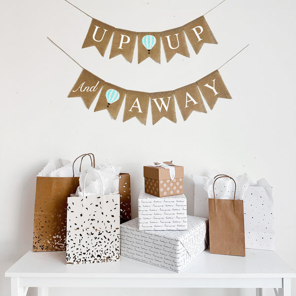 This two tiered Up Up & Away banner add a whimsical touch to your event. The first lay of the banner reads Up Up with a pastel mint striped hot air balloon. The second line starts with the word and stenciled in a script font on one flag followed by another mint hot air balloon and the words Away.