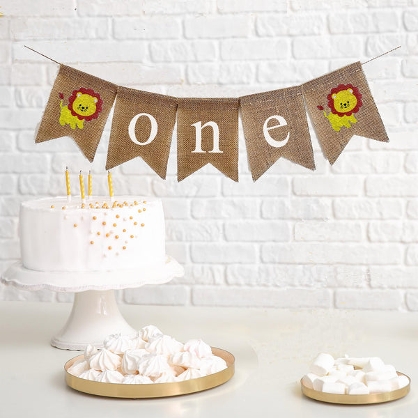 This is a burlap banner made of 5 fishtail shaped flags. The word ONE is spelled out in white lowercase letters on the middle three flags. There is an image of a yellow lion with an orange mane on each end of the banner. The flags measure 4.5 by 6.5 inches each.