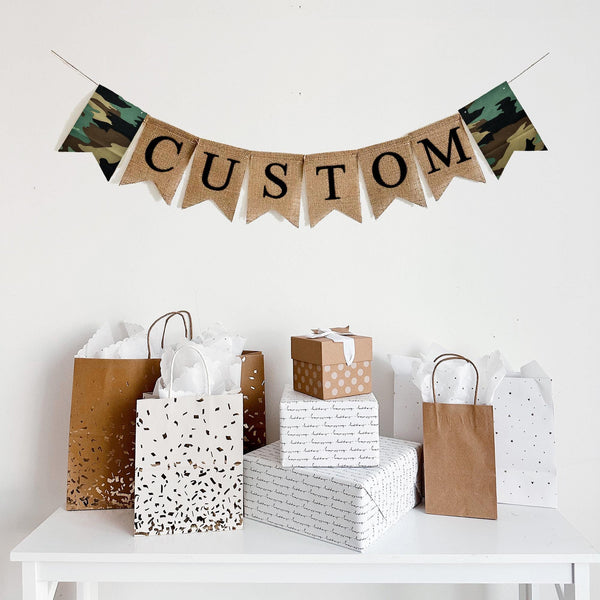 A personalize burlap banner. Printed on burlap fishtail flags with black letters. On each side of the personalized banner there is a fabric camouflage fishtail flag. This banner is available in black letters or white letters.