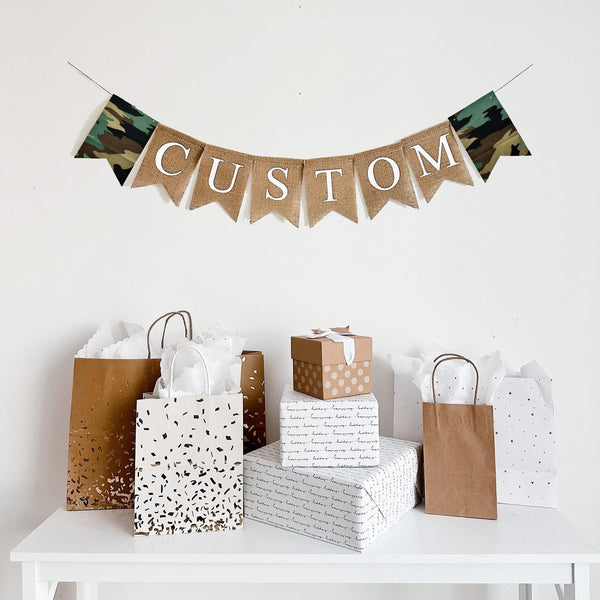 A personalize burlap banner. Printed on burlap fishtail flags with black letters. On each side of the personalized banner there is a fabric camouflage fishtail flag. This banner is available in black letters or white letters.