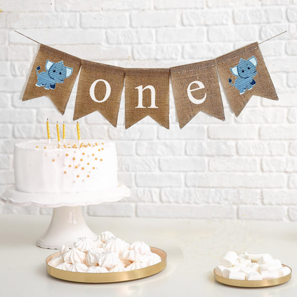 one first birthday banner with grey elephants with white ears on each end. the banner spells out o n e in lowercase white letters on burlap flags.