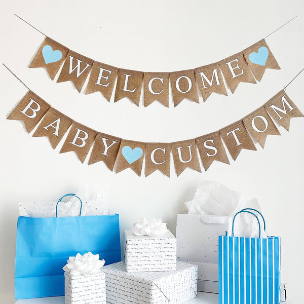 A burlap banner made from 4.5 by 6.5 inch fishtail shaped flags. Each flag has a pocket across the top for stringing. The top line says WELCOME in white capital letters. There is a hand stenciled image of a baby blue heart on each end. The bottom string says BABY CUSTOM and has a hand stenciled image of a baby blue heart between the words. Add your own name to this banner. It is strung on two jute strings that are 110 inches in length.