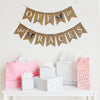 A burlap banner made from 4.5 by 6.5 inch fishtail shaped flags. Each flag has a pocket across the top for stringing. The top string of this banner says OFF in white capital letters and TO in white script one on flag with a hand stenciled image of a horse with a pink saddle in between the words. The bottom string says THE in white script on one flag and RACES  in white capital letters with a hand stenciled horse with pink saddle in between the words. It is strung on two 110 inch jute strings.